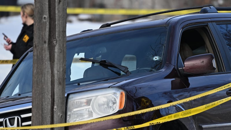 A bullet hole is seen in the windshield as law enforcement officers work at the scene of a...