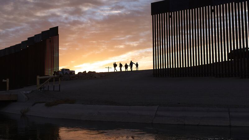 Un par de familias migrantes de Brasil que buscan asilo caminan a través de un hueco en el...