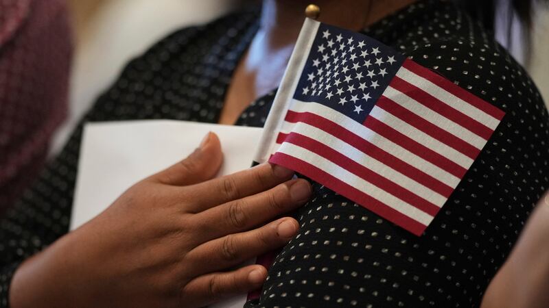 Una mujer abraza una bandera estadounidense mientras ella y otros solicitantes se preparan...