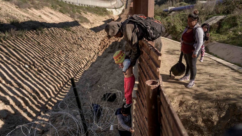 A man passes a Mexican migrant baby to her mother after they jump the border fence to get into...